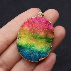 Détail macro du pendentif ovale druzy arc-en-ciel avec bordure dorée tenu en main