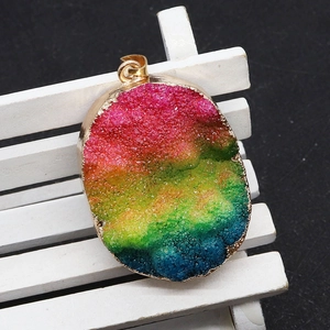 Détail d'un pendentif en cristal druzy arc-en-ciel avec bord doré et fermoir graine