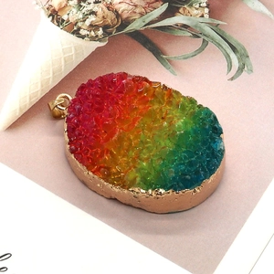 Pendentif druzy ovale arc-en-ciel avec dorure sur fond rose avec fleurs séchées