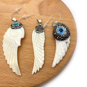 Three natural shell wing pendants with micro-pave diamonds and evil eye details on wood