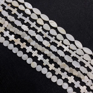 Natural white mother of pearl shell beads in star, leaf and hamsa shapes on black surface