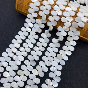 Makro-Detail von weißen Perlmutt-Tropfenperlen mit irisierendem Glanz auf Bambus