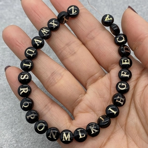 Macro shot of 8mm black shell beads with gold engraved letters for DIY necklaces