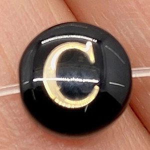 Polished black bead with gold letter C for DIY jewelry making on transparent string
