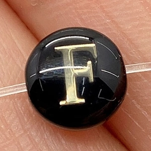 Macro view of a black shell bead featuring a golden letter F for DIY jewelry