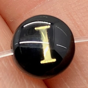 Macro shot of circular black natural shell bead with gold letter I for DIY jewelry