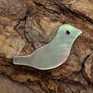 Dettaglio di una perla in madreperla a forma di uccello su sfondo di corteccia naturale