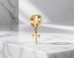 Detail of gold huggie earring with polished cross pendant in hip hop punk style