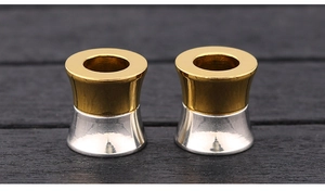 Detail view of two-tone gold and silver stainless steel ear gauges on a wood surface