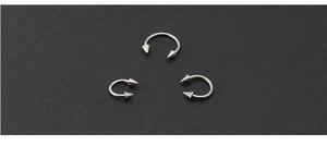 Three horseshoe circular piercing rings with sharp cone ends on a black textured surface
