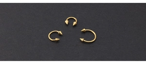 Detailed view of three gold-plated horseshoe piercings with spikes on dark background