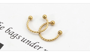 Macro detail of twisted gold steel piercing rings with double ball ends on white background