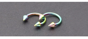 Two rainbow oil slick circular barbells with spiked cone ends on textured grey background