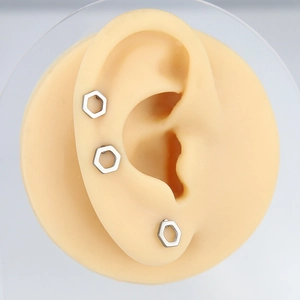 Close-up of three hollow hexagonal stainless steel stud earrings on a silicone ear model