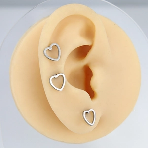Detailed view of three minimalist silver heart-shaped stud earrings on a silicone ear model