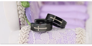 Close-up of black stainless steel huggie earrings featuring a silver cross design