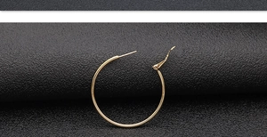 Detailed view of large gold-plated hoop earrings with polished surface on a dark textured background