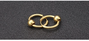 Macro detail of polished gold titanium steel ball closure rings showing smooth metal texture