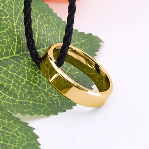 Goldener polierter Edelstahlring mit abgeschrägten Kanten und schwarzer Kordel auf Weiß