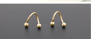 Macro shot of gold-plated spiral piercing rings with spherical ends on a dark background
