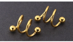 Macro shot of gold spiral eyebrow rings with polished metal balls on a dark surface