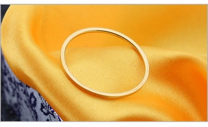 Detailaufnahme eines minimalistischen Goldrings mit Hochglanzpolitur auf gelbem Stoff