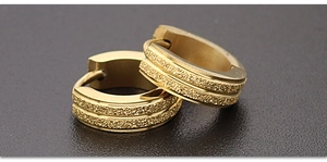 Nahaufnahme goldener Edelstahl-Creolen mit glitzernder, mattierter Sand-Oberfläche