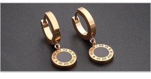 Close-up of rose gold titanium earrings featuring Roman numerals and black disk pendants