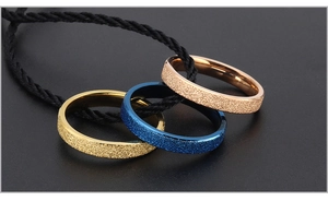 Macro shot of three frosted titanium steel rings in gold, blue, and rose gold on black cord