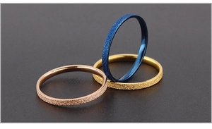 Detailed view of three stackable frosted stainless steel rings in gold, blue, and rose gold