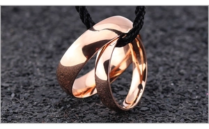 Macro shot of interlocking rose gold titanium rings with polished finish on a black cord