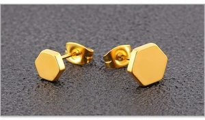 Vue macro de boucles d'oreilles hexagonales dorées avec fermoirs papillon sur fond noir
