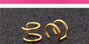 Vue macro de boucles d'oreilles clips en acier doré forme double C sur fond texturé noir