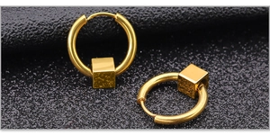 Macro shot of gold stainless steel hoop earrings featuring a minimalist cube pendant detail