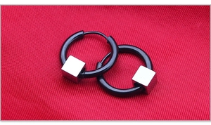 Detail of black hoop earrings with polished silver cube charm on red textured fabric