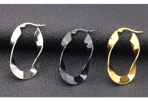 Detail van grote gedraaide roestvrijstalen oorringen in zilver, goud en zwart