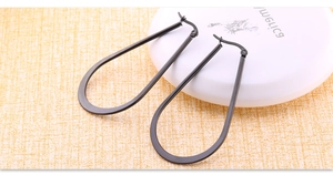 Detail of large black stainless steel teardrop hoop earrings with matte finish texture