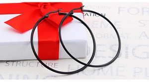 Close-up of matte black stainless steel hoop earrings next to a white gift box with red ribbon