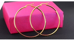 Detailed close-up of large polished gold hoop earrings on a decorative pink jewelry box
