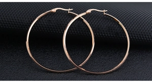 Detailed close-up of large rose gold stainless steel hoop earrings on a black textured background