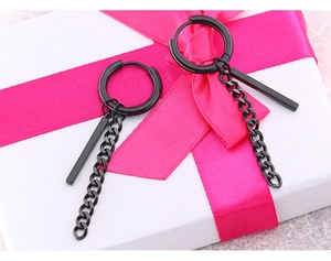 Detail von schwarzen Edelstahl-Ohrringen mit Kette und Stab auf einer Geschenkbox