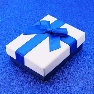 Dettaglio di una scatola regalo per gioielli blu e bianca con fiocco su sfondo glitterato
