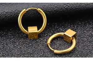 Detailansicht goldener Creolen mit geometrischem Würfelanhänger auf schwarzem Grund