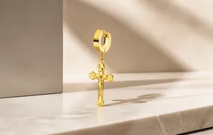 Primer plano del pendiente de cruz en acero dorado con relieve detallado de Jesús tallado