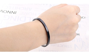 Polished minimalist black stainless steel bangle shown worn on a wrist for styling