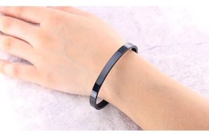 Minimalist black stainless steel open cuff bracelet on female wrist with a glossy finish
