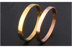 Detail shot of gold and rose gold oval hinged bangles on black leather surface