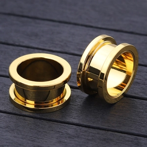 Pair of polished gold stainless steel double flared ear tunnels on dark wood surface