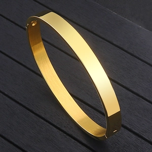 Polished gold stainless steel oval cuff bracelet on elegant black wood texture background