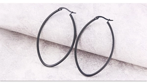 Detail of large oval hoop earrings in matte black finish on marble stone background